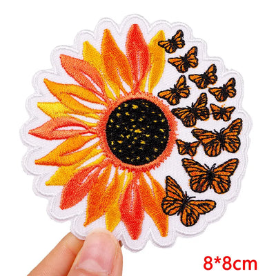 Embroidered patch with a sunflower and butterflies held by a hand on a white background.