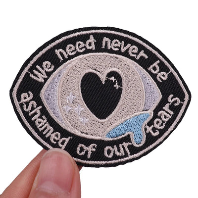 Embroidered patch with a heart and text held by a hand on a white background