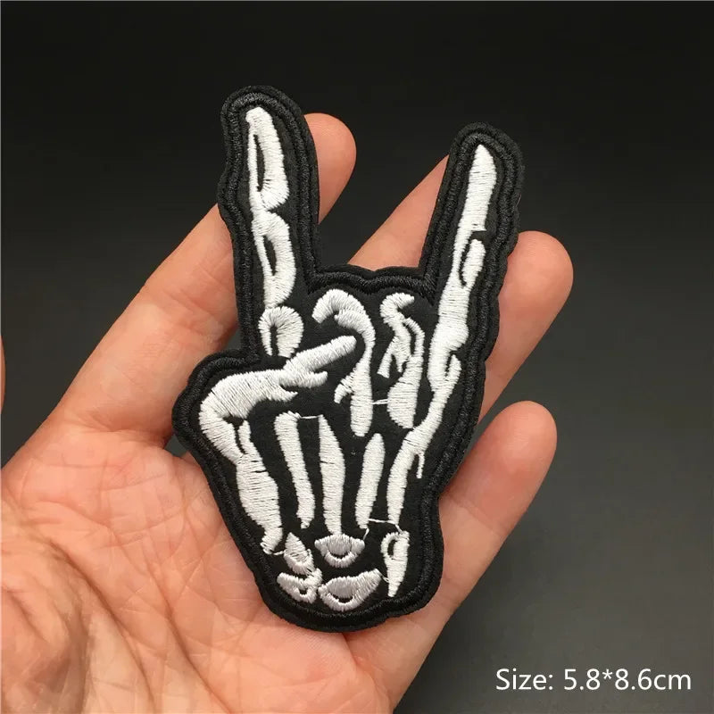 Hand holding a black and white skeleton hand patch with a peace sign on a dark background