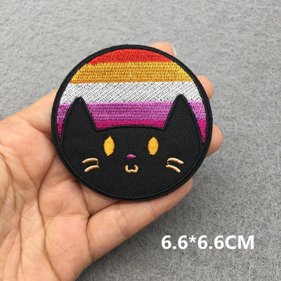 Black cat patch with rainbow stripes held in a hand on a gray background