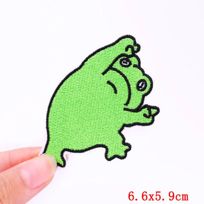 Green cartoon frog patch held by a hand on a white background