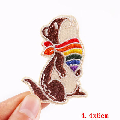 Squirrel patch with rainbow scarf held by a hand on a white background