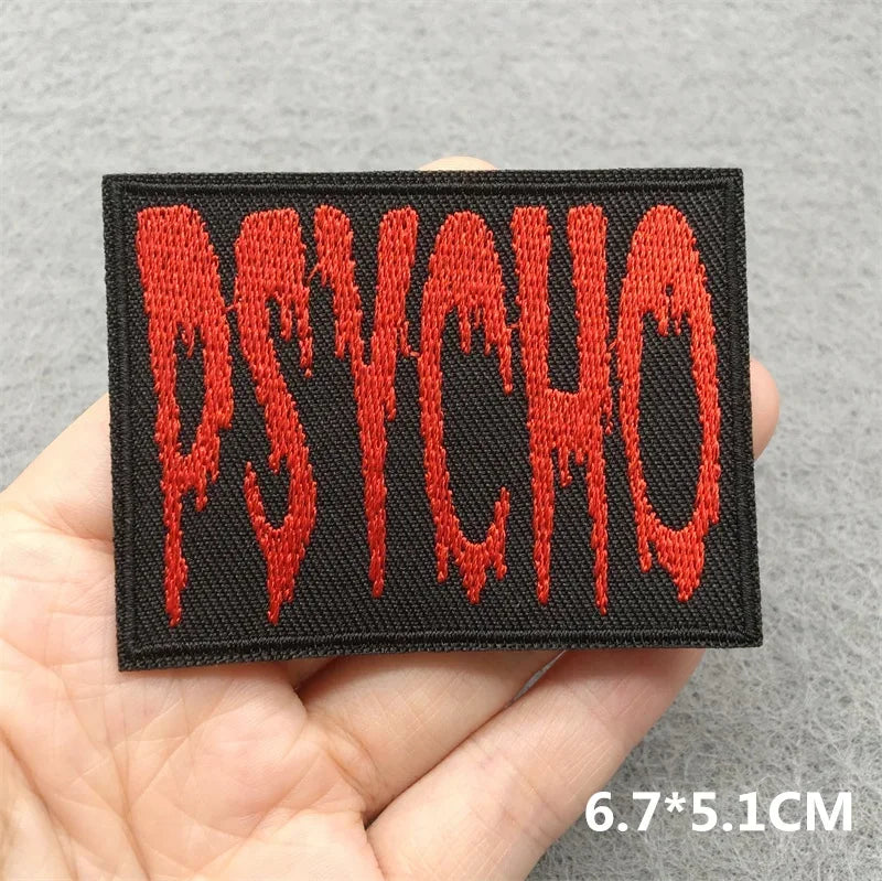 Embroidered patch with 'PSYCHO' in red on a black background held in a hand against a gray background.