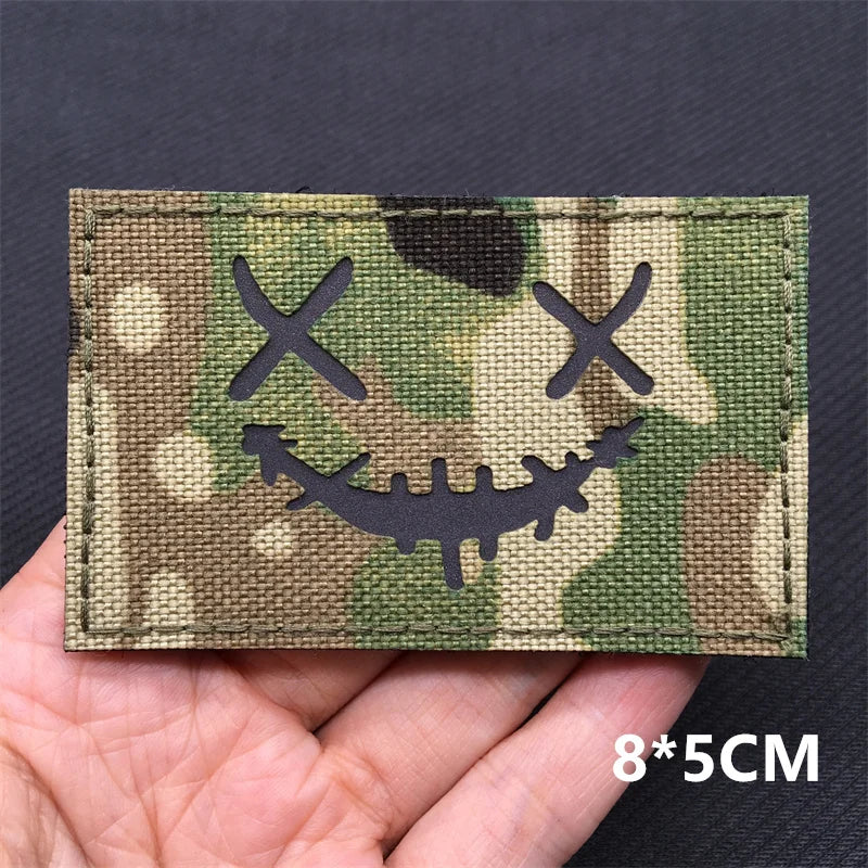 Camouflage patch with a smiley face design held in a hand against a dark background