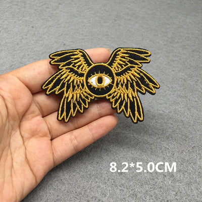 Embroidered patch with wings and an eye held in a hand on a gray background