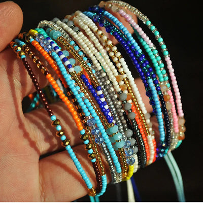 Hand holding a stack of colorful beaded bracelets against a dark background