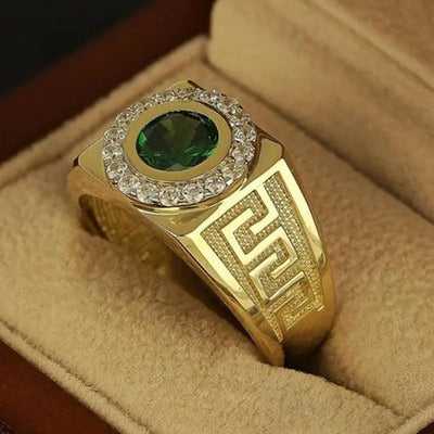 close up Elegant gold tone ring with  green gemstone at the center, surrounded by small zircon, featuring a geometric pattern on the band, resting in a velvet box.