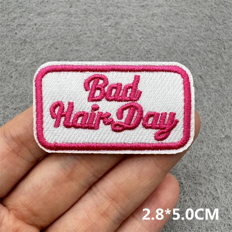 Embroidered patch with 'Bad Hair Day' text held by a hand on a gray background