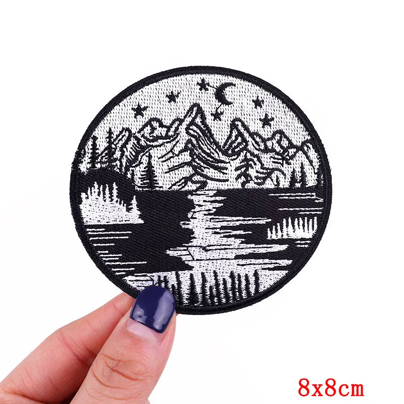 Circular patch with mountain and deer design held by a hand on a white background