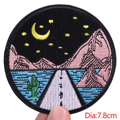 Embroidered patch with a night scene design held by a hand, showing a road, mountains, and moon.
