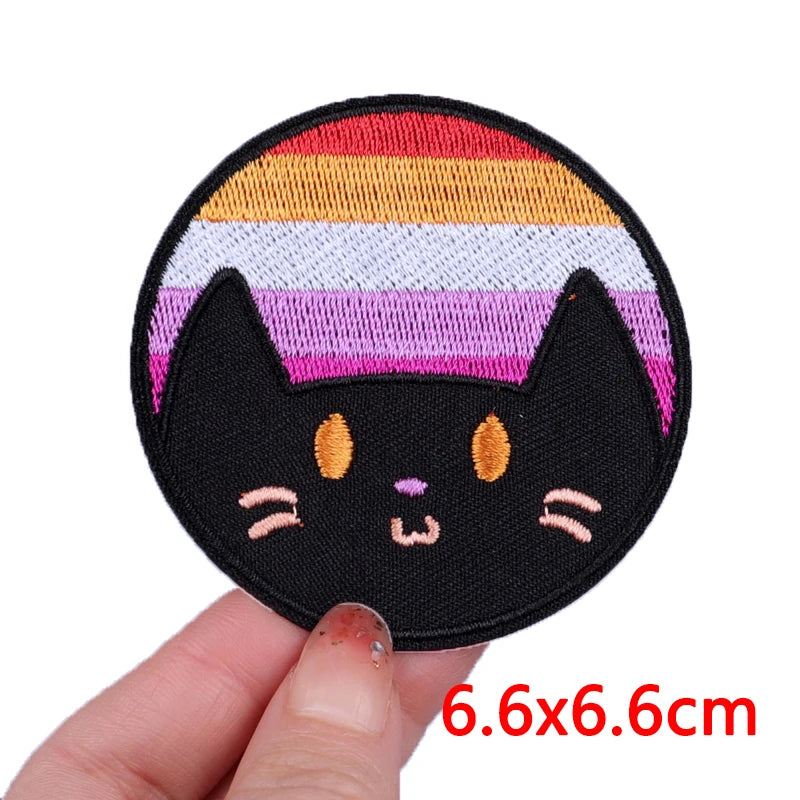 Black cat patch with rainbow stripes held by a hand, size 6.6x6.6cm.