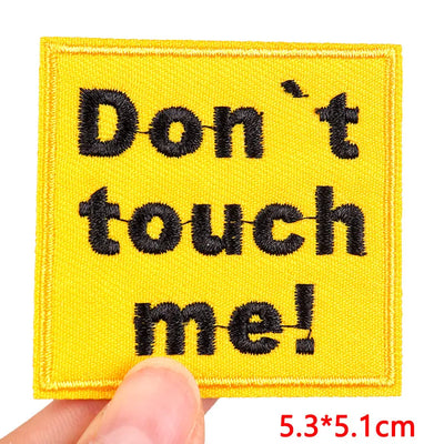 Yellow patch with black text 'Don't touch me!' held by a hand on a white background.