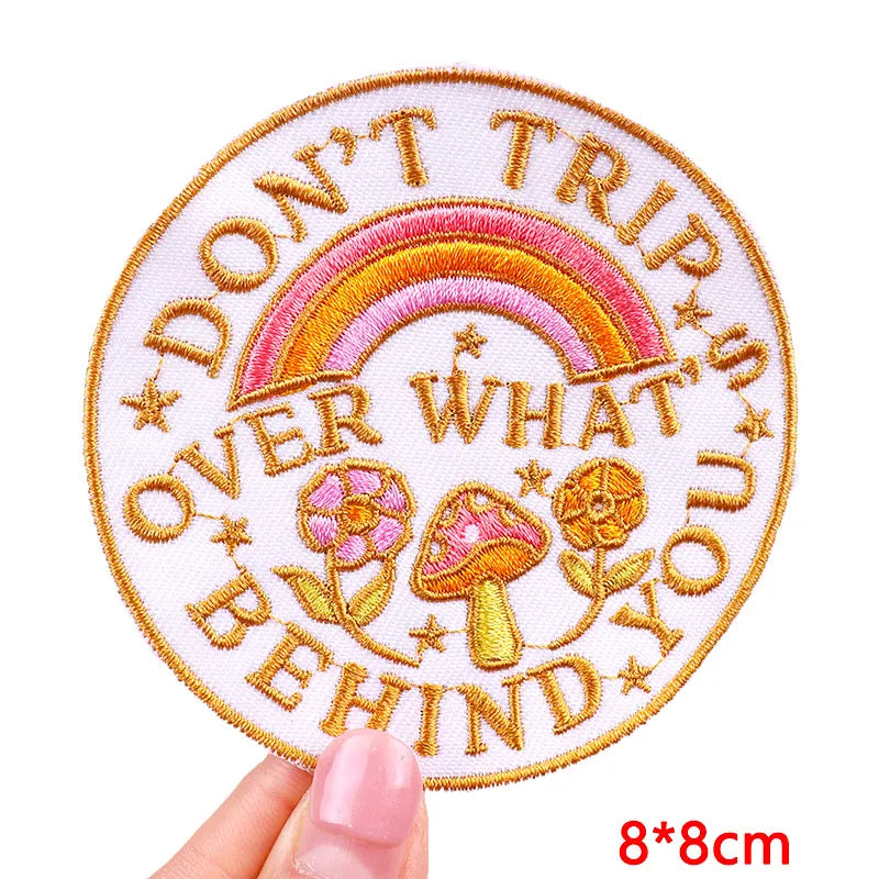 Embroidered patch with rainbow, mushrooms, and text held by a hand on a white background