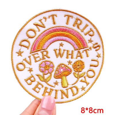 Embroidered patch with rainbow, mushrooms, and text held by a hand on a white background