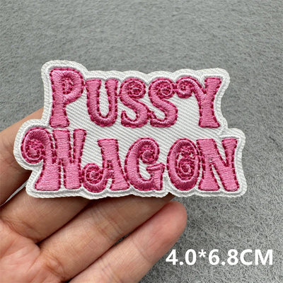 Embroidered patch with 'PUSSY WAGON' text held by a hand on a gray background