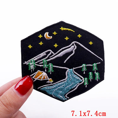 Embroidered patch with mountain and camping scene held by a hand on a white background