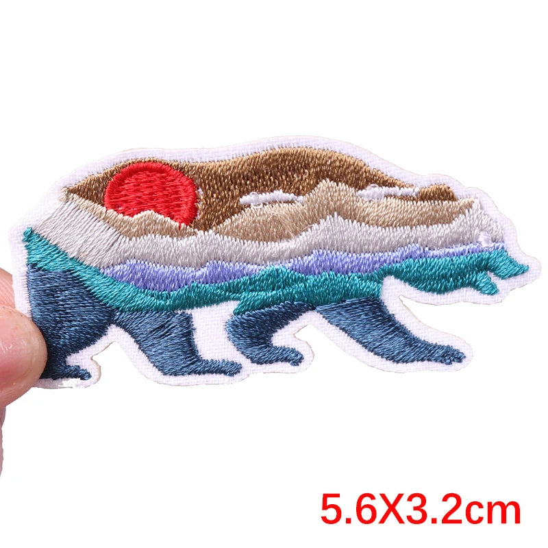 Embroidered patch of a desert landscape with a red sun held by a hand on a white background.