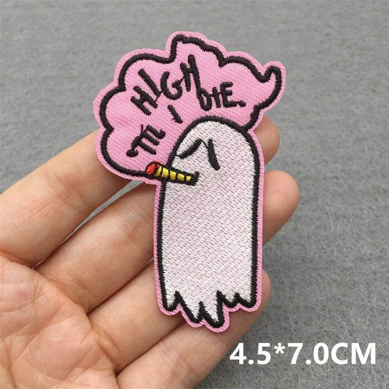 Embroidered patch of a ghost smoking with 'High the I Die' text on a pink cloud held in a hand against a gray background.