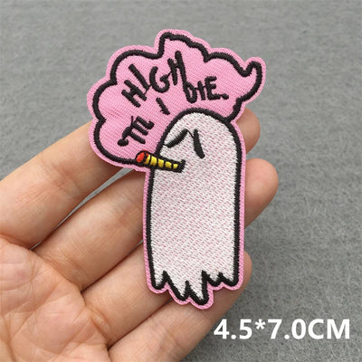 Embroidered patch of a ghost smoking with 'High the I Die' text on a pink cloud held in a hand against a gray background.