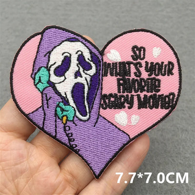 Heart-shaped patch with skeleton design and text held by a hand on a gray background