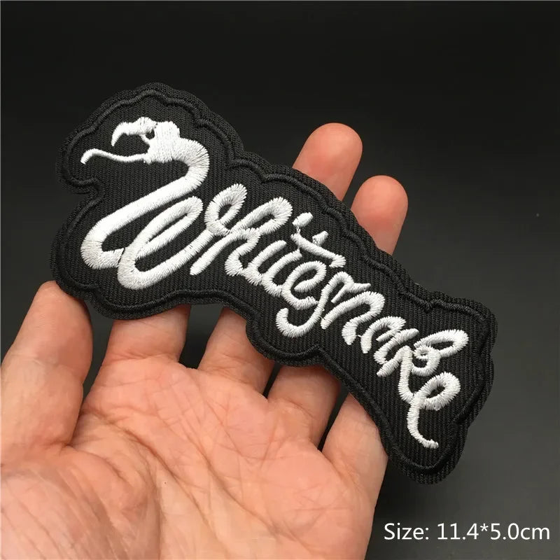 Hand holding a black and white Whitesnake embroidered iron-on patch 11.4x5cm on a dark background