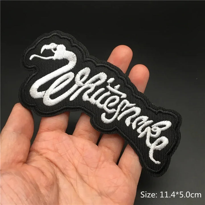 Hand holding a black and white Whitesnake embroidered iron-on patch 11.4x5cm on a dark background