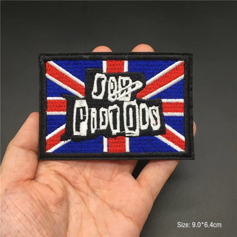 Hand holding a Sex Pistols embroidered iron-on patch with Union Jack background 9x6.4cm on a dark background