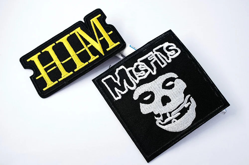 Two patches, one with 'HIM' in yellow and the other with a skull design and text, on a white background.