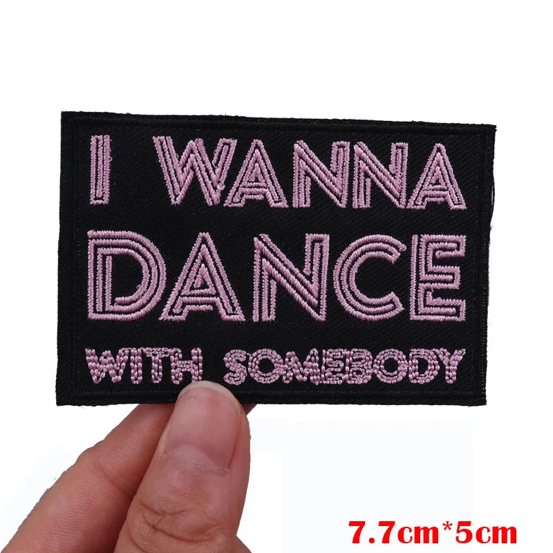 Embroidered patch with 'I WANNA DANCE WITH SOMEBODY' text held by a hand.