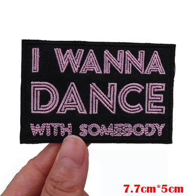 Embroidered patch with 'I WANNA DANCE WITH SOMEBODY' text held by a hand.