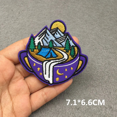 Embroidered patch with mountain and road design held by a hand on a gray background