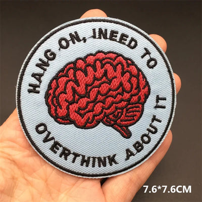 Patch with red brain illustration and text 'Hang on, I need to overthink about it' held in a hand.