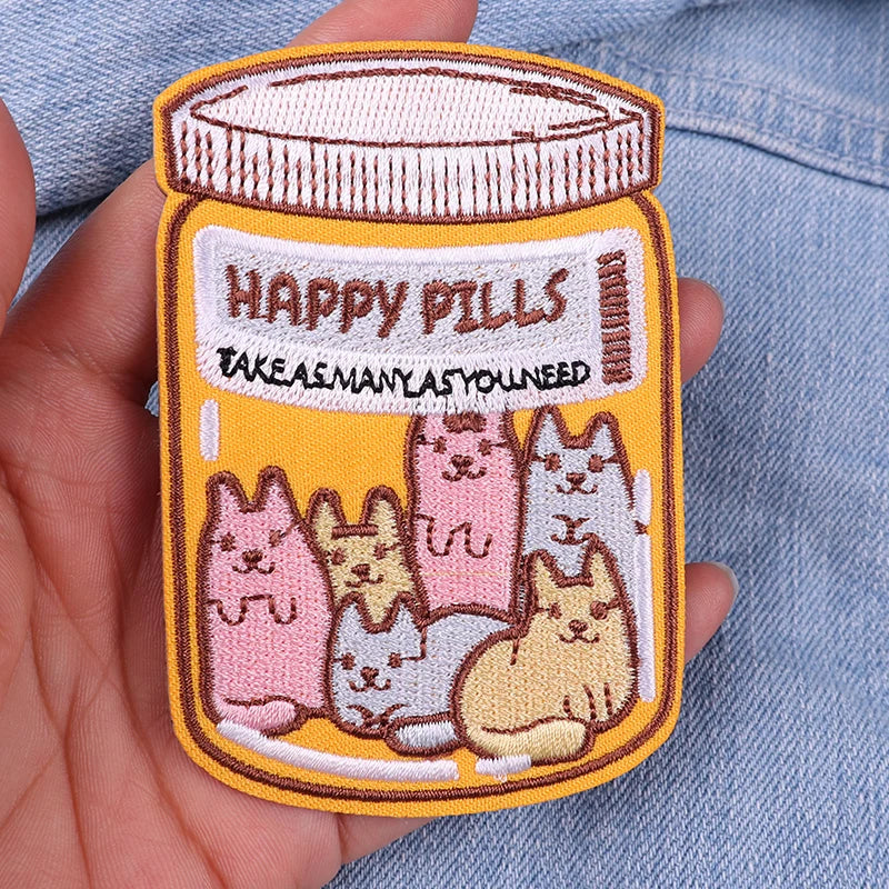 Embroidered patch of a jar labeled 'Happy Pills' with cartoon cats on a denim background