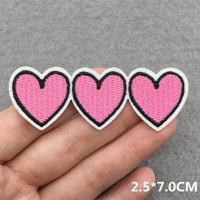 Three pink heart-shaped patches held between fingers on a gray background