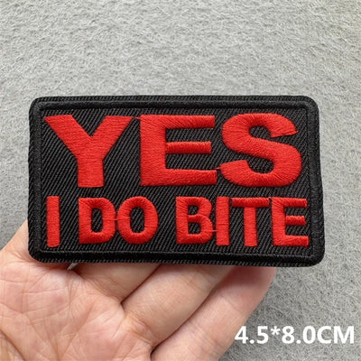 Embroidered patch with 'YES I DO BITE' text held in a hand against a gray background
