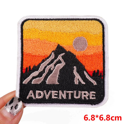 Embroidered patch with mountain design and 'ADVENTURE' text, held by a hand.
