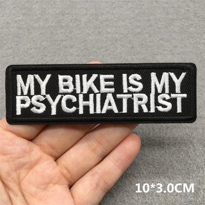 Embroidered patch with text 'My bike is my psychiatrist' held by a hand on a gray background.