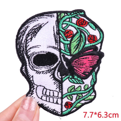 Embroidered patch with skull design, roses, and a butterfly held by a hand on a white background.