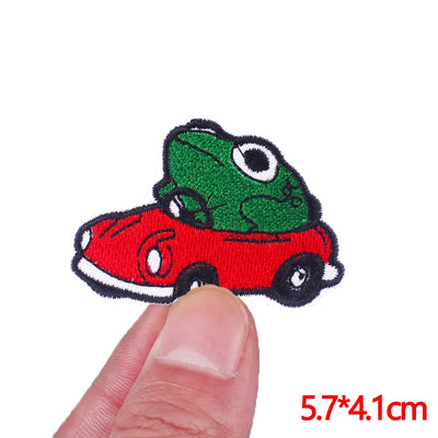 Embroidered patch of a green frog in a red car held between fingers with size label '5.7*4.1cm'.