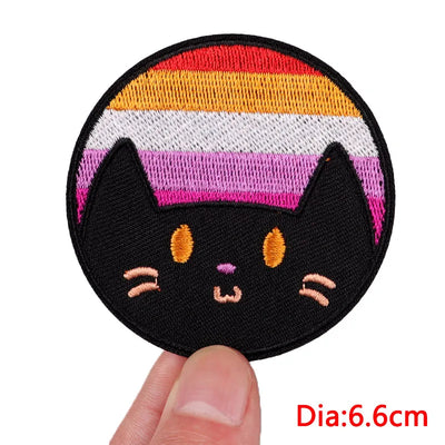 Black cat face patch with rainbow stripes held by a finger on a white background