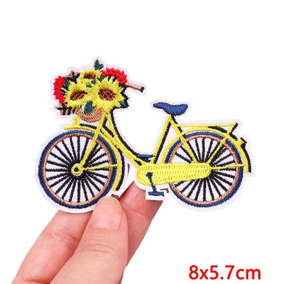 Embroidered patch of a person on a bicycle with flowers, held by a hand.
