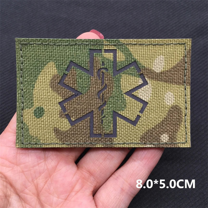 Camouflage patch with medical symbol held in a hand against a dark background