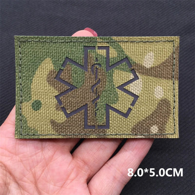 Camouflage patch with medical symbol held in a hand against a dark background
