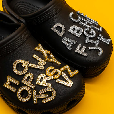 Black clogs with rhinestone letters shoe charms on a yellow background