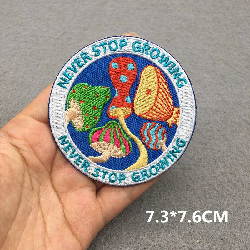 Colorful patch with mushroom design and 'Never Stop Growing' text held in a hand on a gray background.