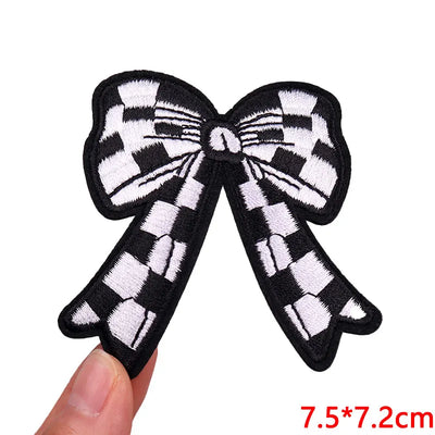Black and white checkered bow patch held by a hand with size measurement on a white background