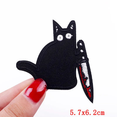 Black cat-shaped patch with a knife design held by a hand on a white background