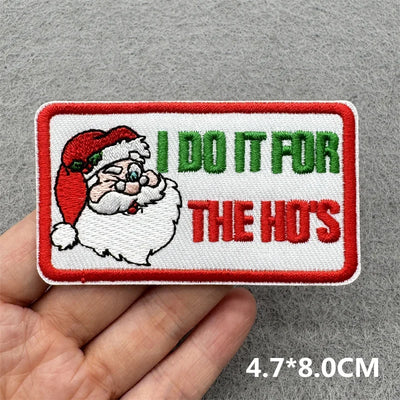 Embroidered patch with Santa Claus and text 'I DO IT FOR THE HO'S' held by a hand on a gray background.