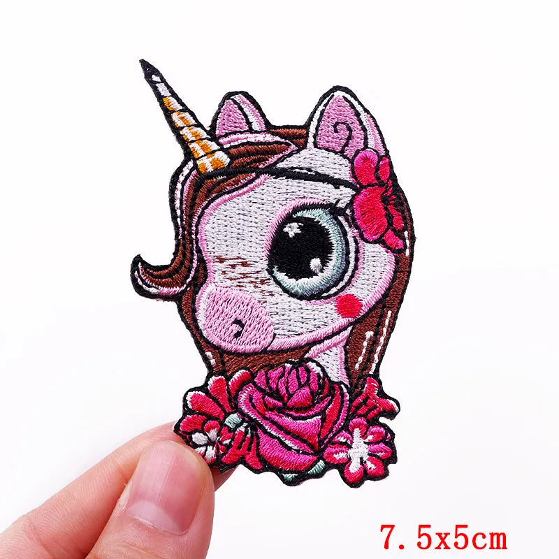 Unicorn patch with pink mane and flowers held by a hand on a white background