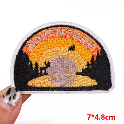 Embroidered patch with 'ADVENTURE' text and landscape design held by a hand.